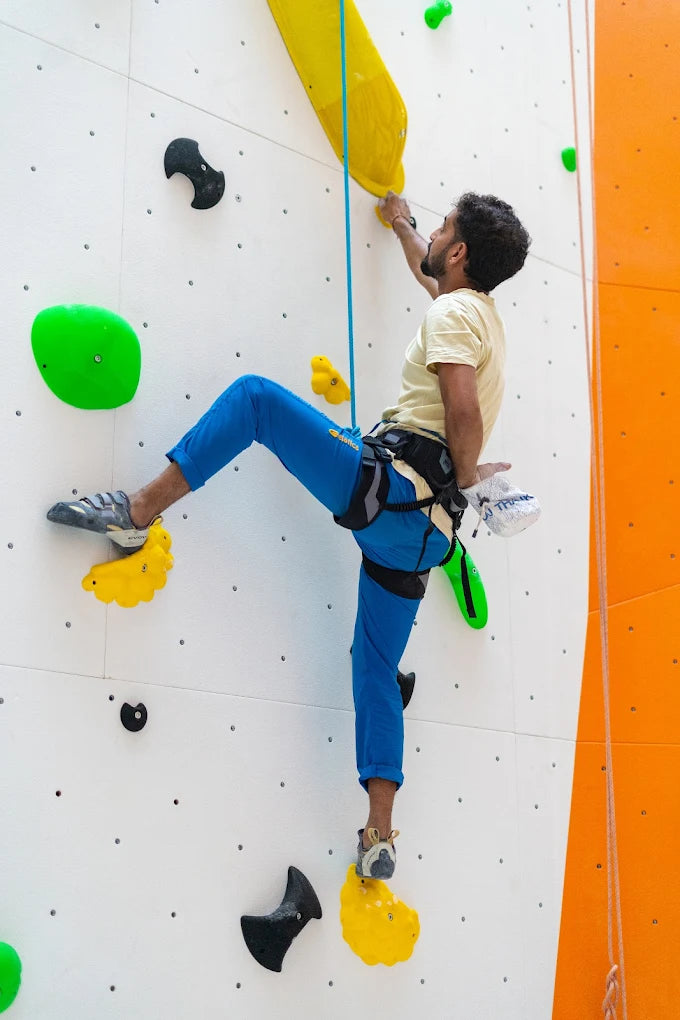 A man climbs a white indoor climbing wall with colorful holds.