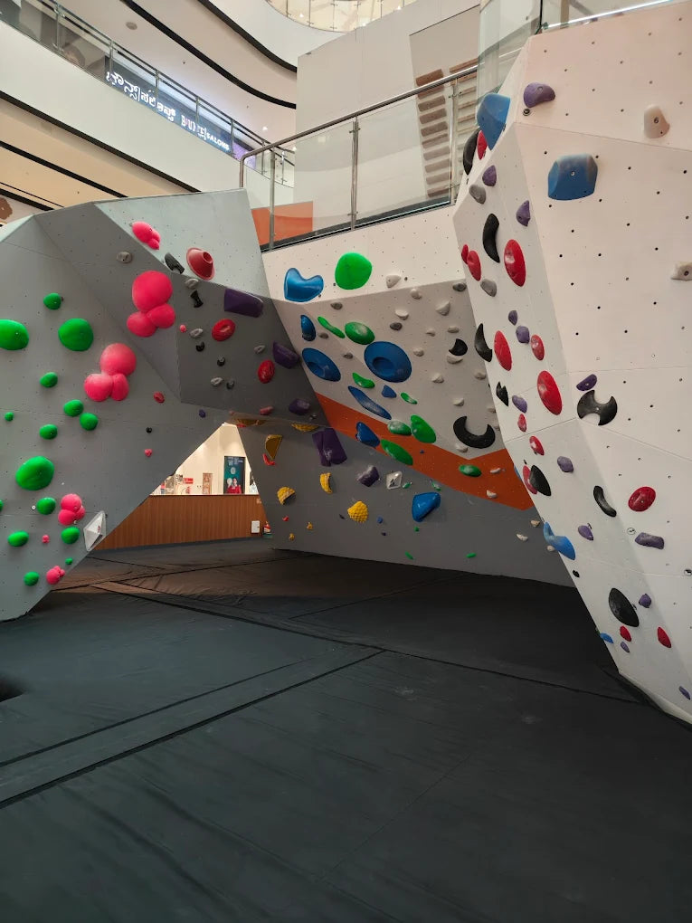 A bouldering gym with colorful holds on angled walls and a padded floor.