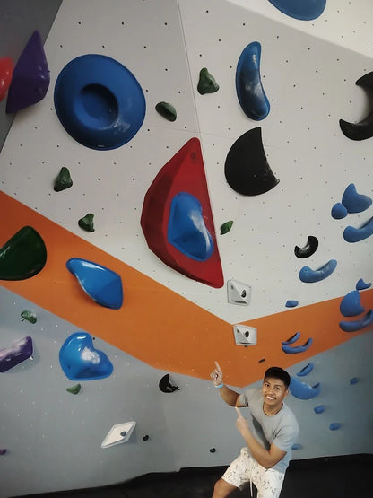 A young man points to a climbing wall with colorful holds.