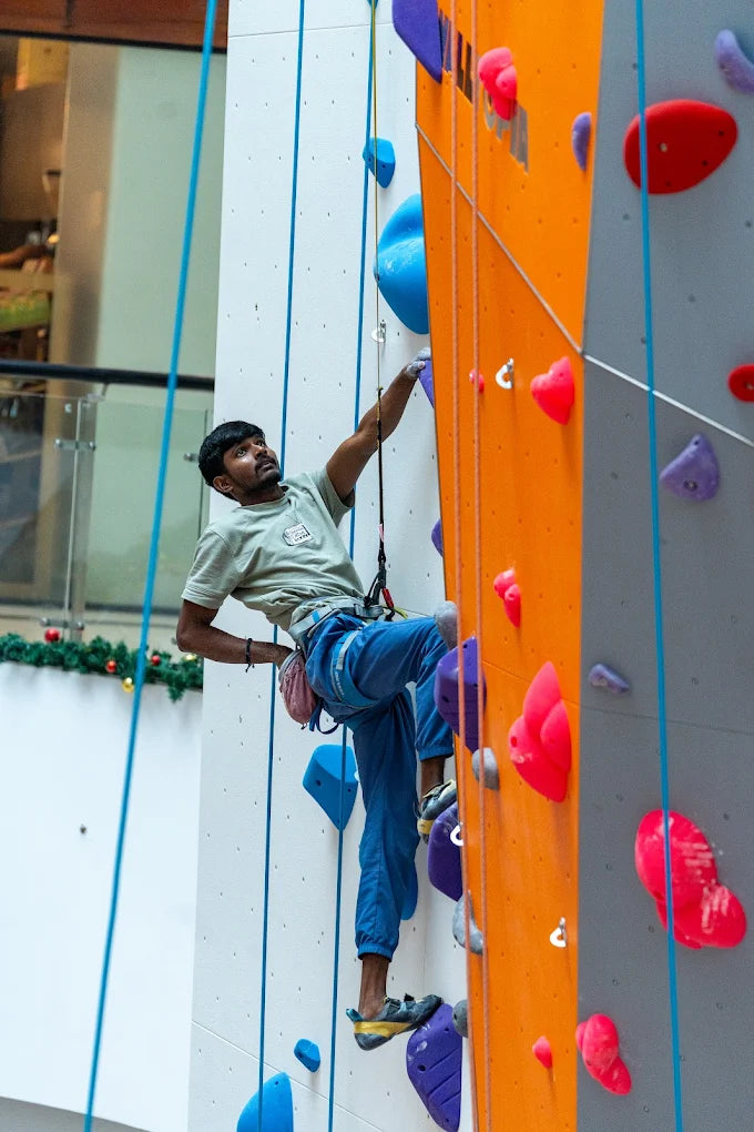 A young man climbs an indoor rock wall, reaching for a hold.