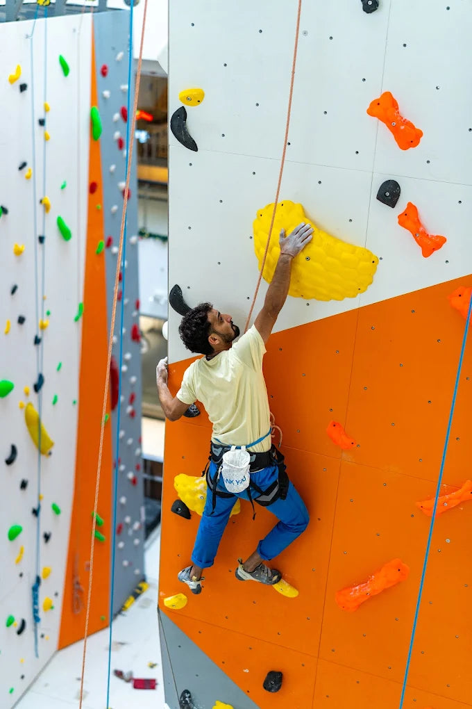 A man climbs an indoor rock wall, reaching for a yellow hold.