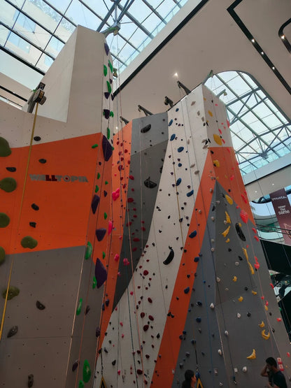 A tall indoor climbing wall with colorful holds, with young people preparing to climb.