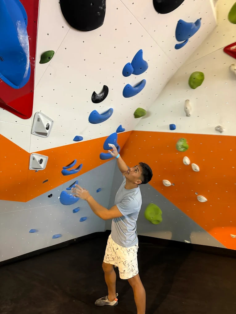 A young man climbs an indoor bouldering wall with colorful holds.