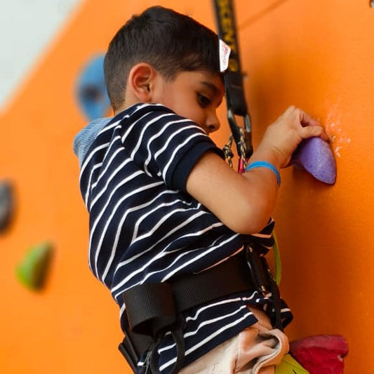 A young boy in a striped shirt climbs an orange wall, using a purple handhold.