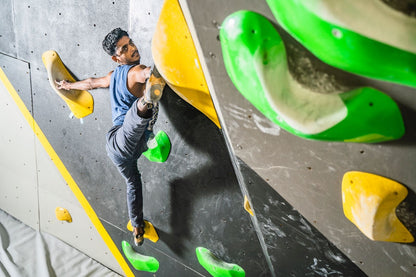 Man skillfully ascending an indoor bouldering wall featuring bright green and yellow holds at Sector 132 Noida facility