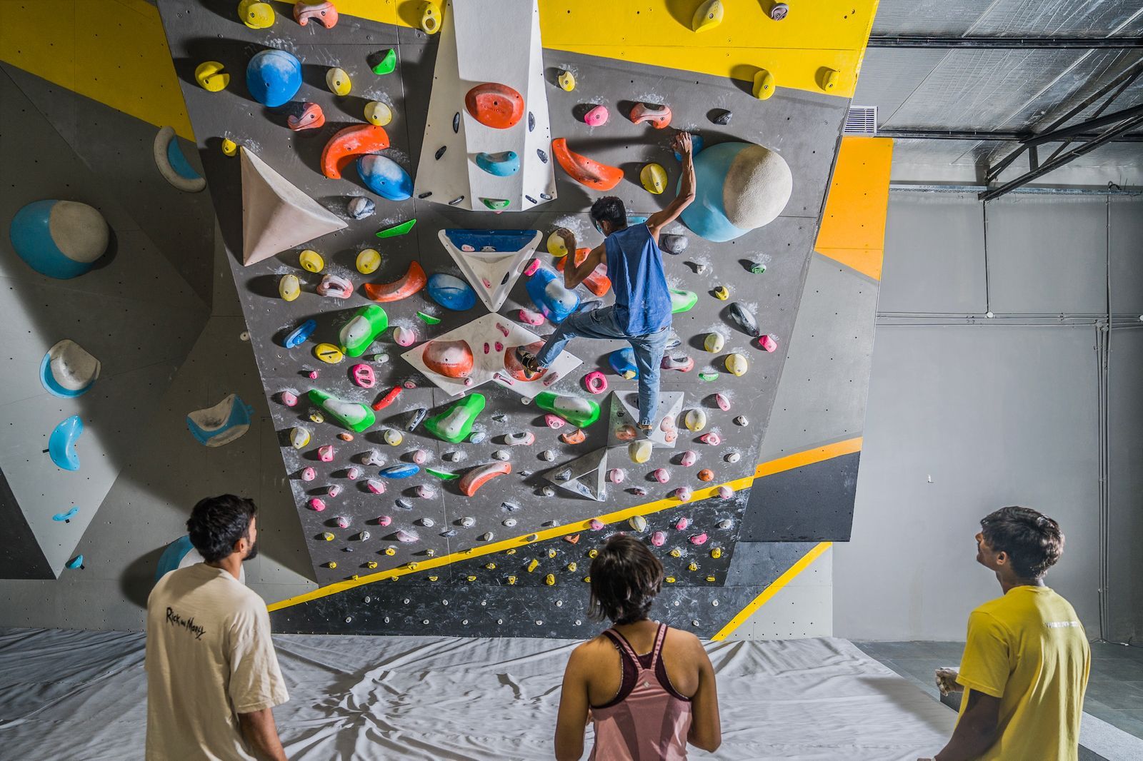 People climbing on an indoor rock climbing wall with colorful holds.