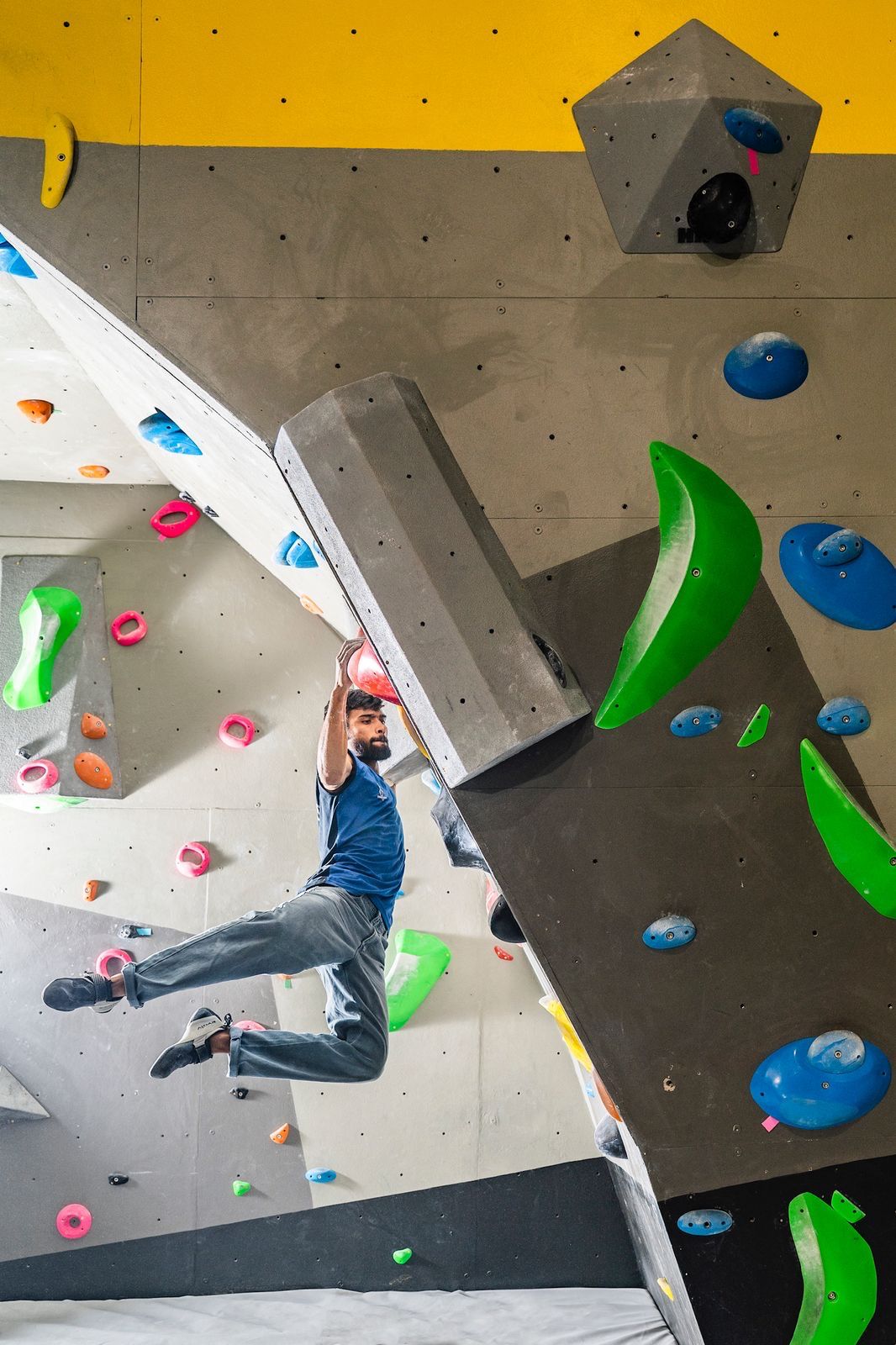 Athletic man navigating a challenging indoor climbing wall with large green and blue holds at Sector 132 Noida facility