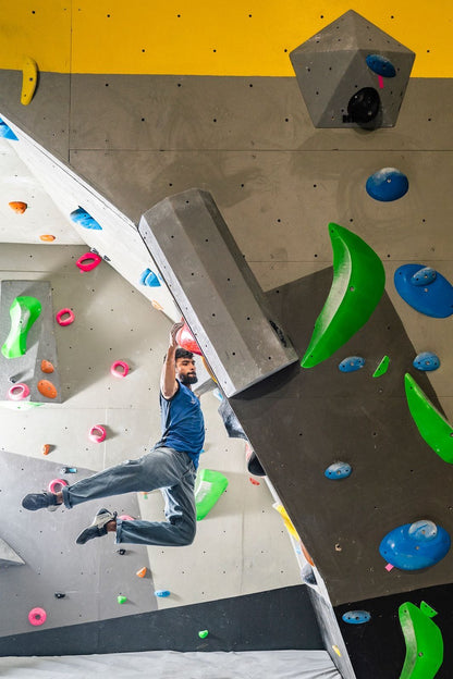 Athletic man navigating a challenging indoor climbing wall with large green and blue holds at Sector 132 Noida facility