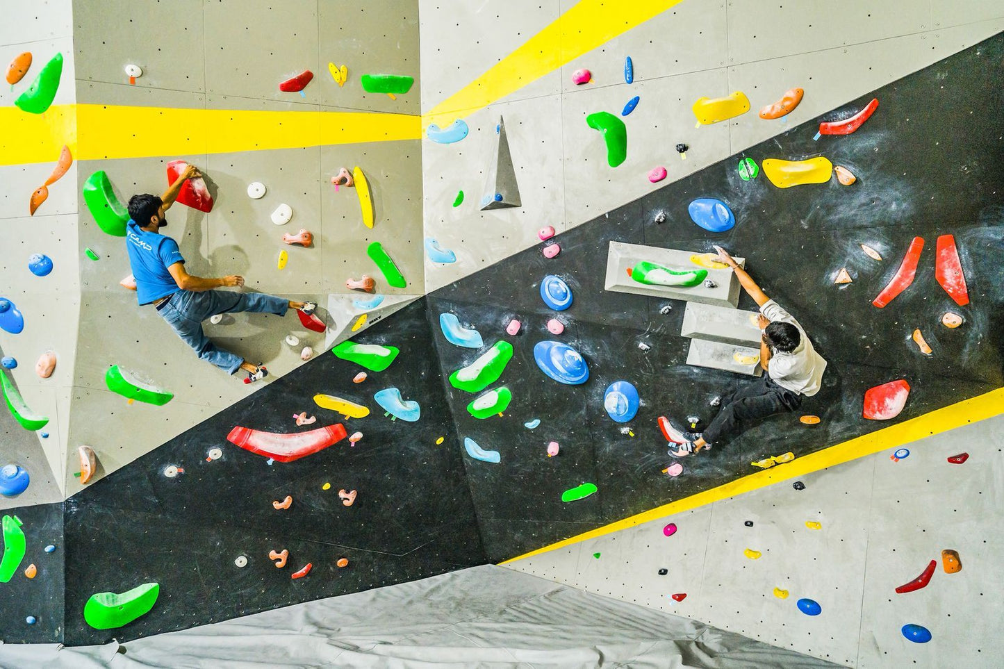Two climbers on an indoor climbing wall with colorful holds.