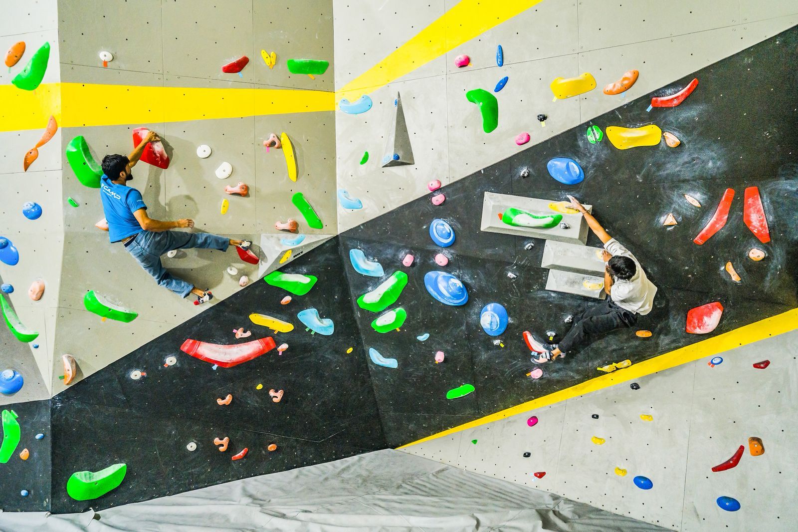 Two climbers on an indoor climbing wall with colorful holds.