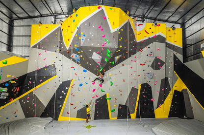 Indoor rock climbing wall with vibrant handholds and climbers practicing in a spacious facility at Sector 132 Noida