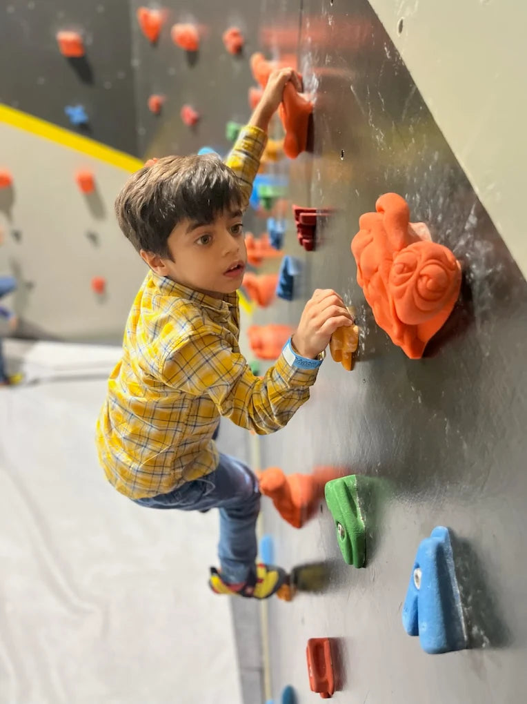 Child climbing on an indoor rock climbing wall with colorful holds.