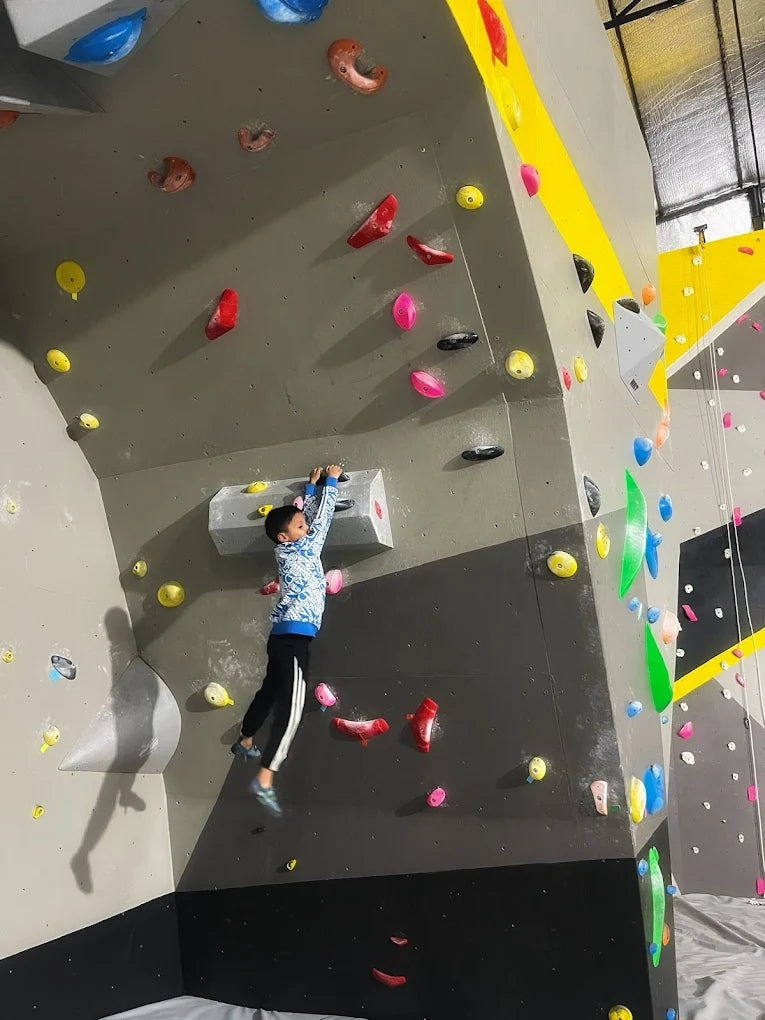 Young climber reaching for holds on an indoor rock wall with colorful grips at Climb City Sector 132 Noida