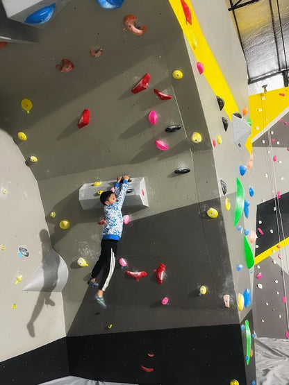 Young climber reaching for holds on an indoor rock wall with colorful grips at Climb City Sector 132 Noida