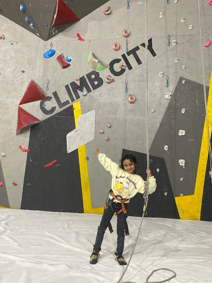 Child smiling and holding climbing rope in front of climbing wall at Climb City indoor facility in Sector 132 Noida