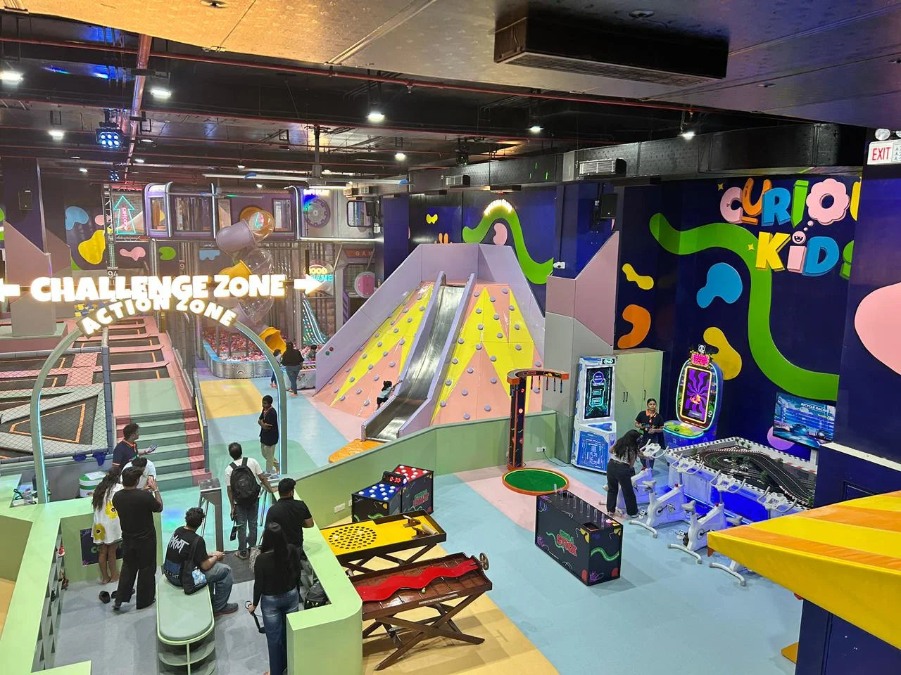 A vibrant indoor play area for children with slides, trampolines, and arcade games, filled with families.