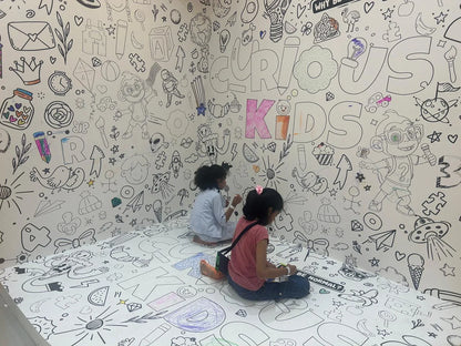 Two young children color on a wall and floor covered in black and white drawings.