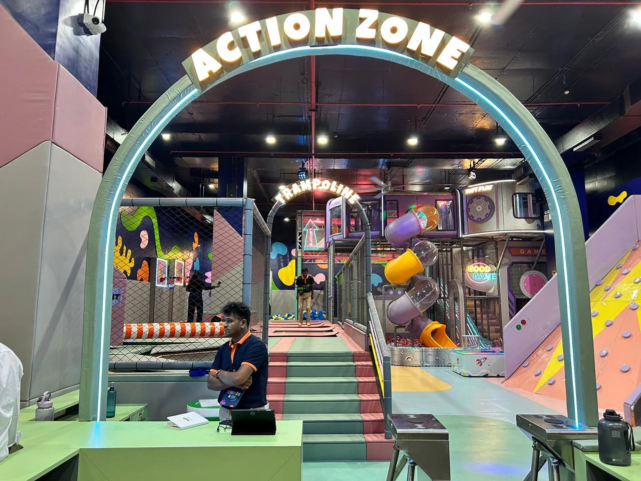 An indoor adventure park with trampolines, slides, and climbing walls, featuring young people playing.