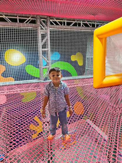 A young boy stands on a pink net floor in a colorful indoor playground.