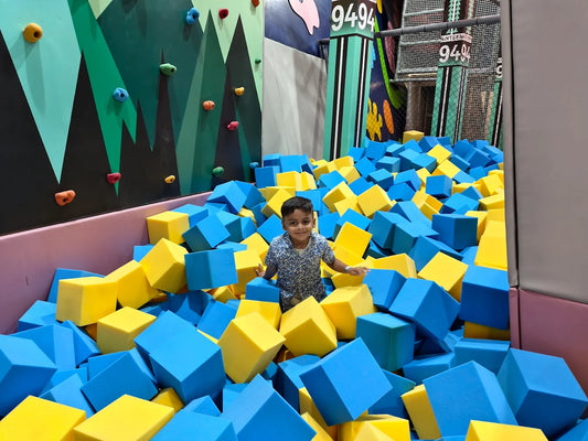 A young boy smiles from a foam pit filled with blue and yellow cubes.