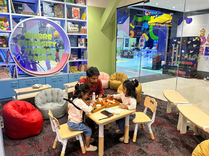 A father and two young daughters play at a table in a colorful, child-friendly library.