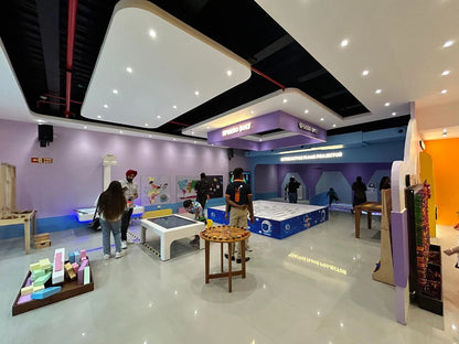 People interact with exhibits in a brightly lit, modern science museum with colorful walls and interactive displays.