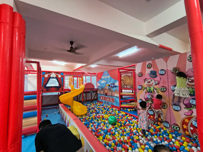 Children play in a colorful indoor circus-themed playground with a ball pit and climbing wall.