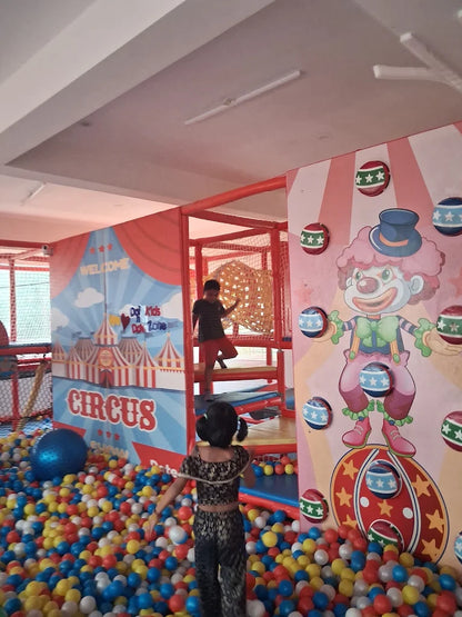 Children play in a colorful indoor circus-themed play area with a ball pit and climbing structures.
