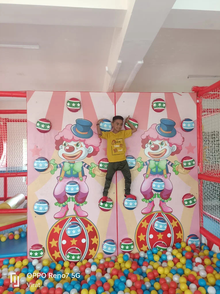 A young boy climbs on a wall with clown graphics in a ball pit.