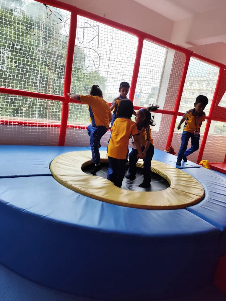 Children in school uniforms play on a trampoline in an indoor play area.