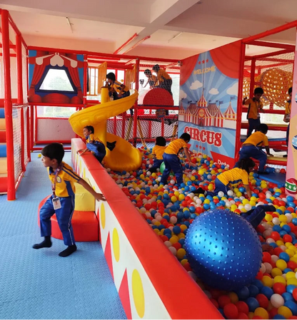 Children play in a colorful indoor playground with slides and a ball pit, decorated with a circus theme.