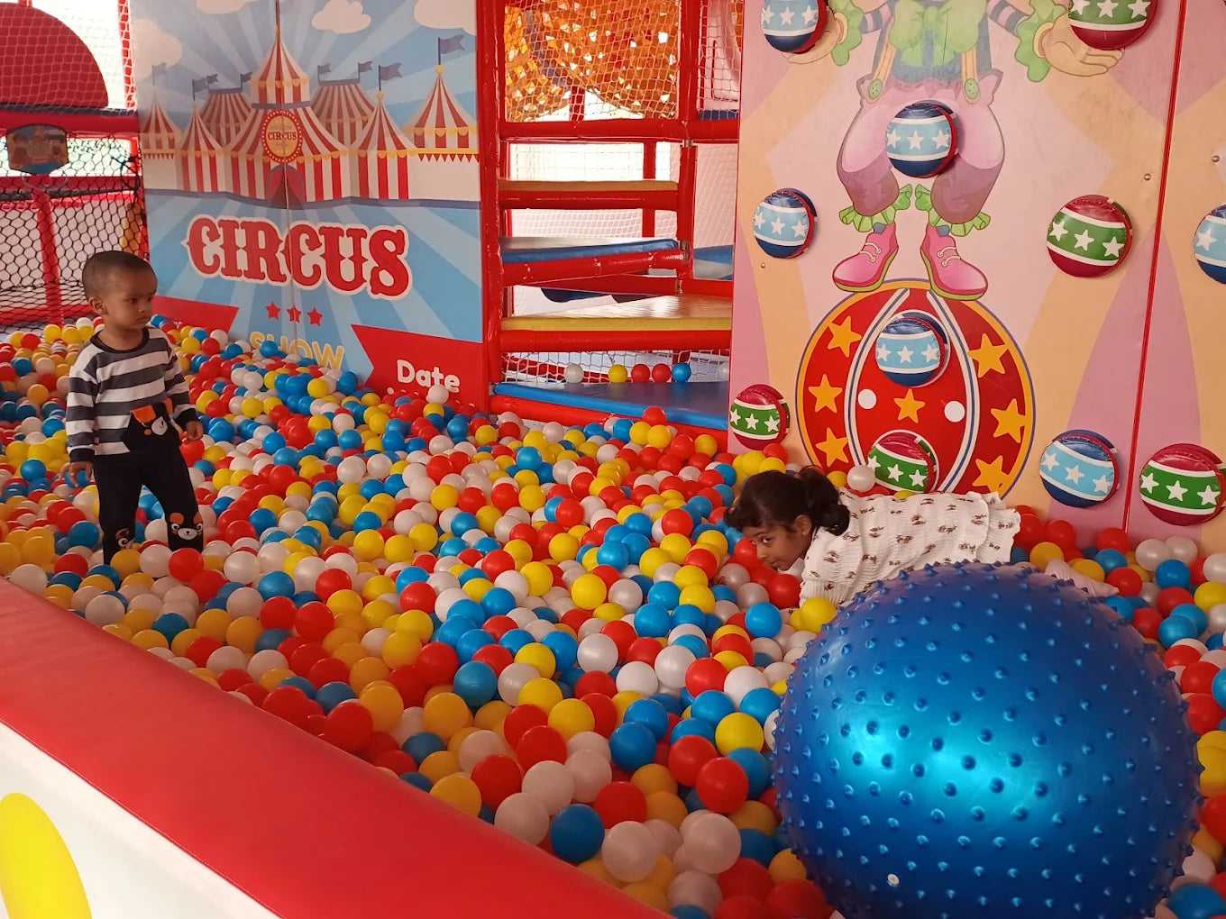 Children play in a colorful ball pit at a circus-themed indoor playground.