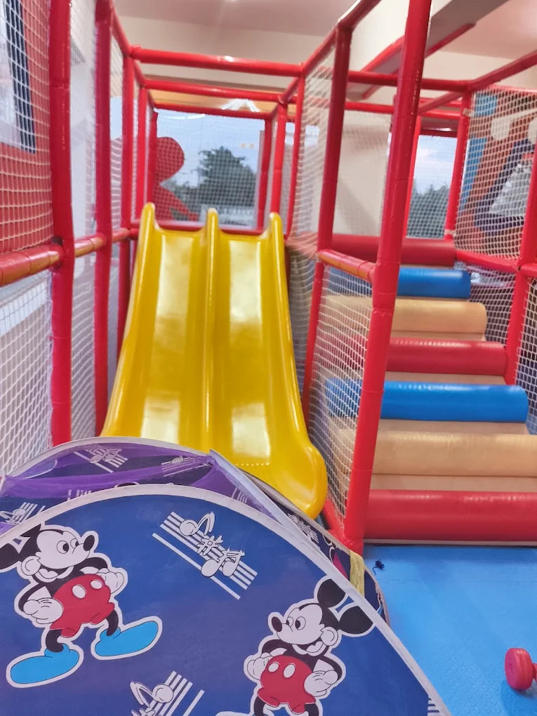A yellow double slide in a red and blue indoor playground with Mickey Mouse decorations.
