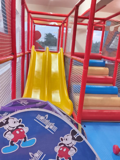 A yellow double slide in a red and blue indoor playground with Mickey Mouse decorations.