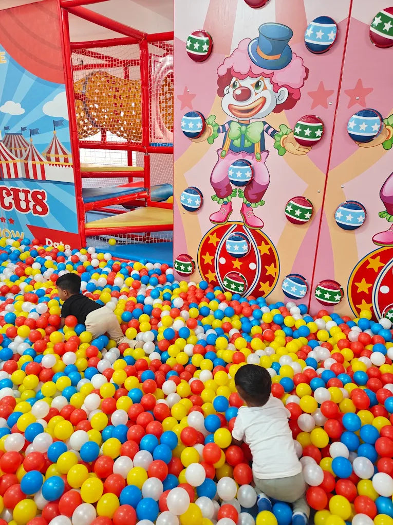 Children play in a colorful ball pit at a circus-themed indoor playground.