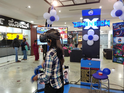 A young person plays a VR game in a mall, with others watching.