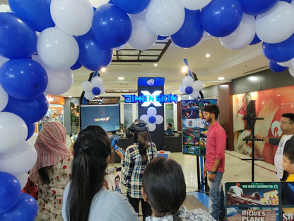 Young people play a VR game at a mall event decorated with blue and white balloons.