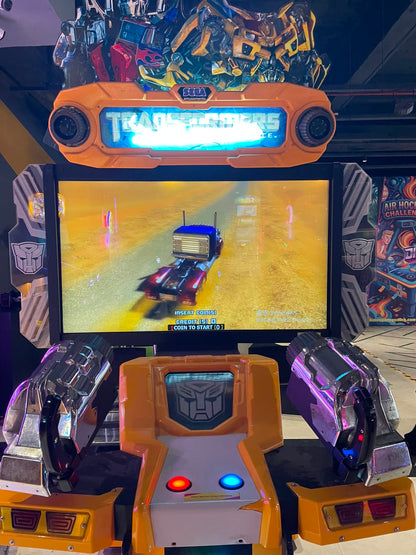An arcade game cabinet for Transformers, featuring a screen displaying the game and two toy guns.