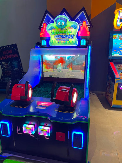 A "Zombie Outbreak" water shooting arcade game with two players aiming water guns at a screen showing a zombie in a burning city.