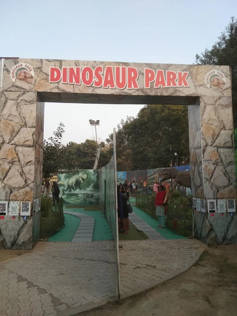 Entrance to a dinosaur park with a large sign and people walking through.