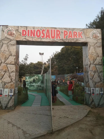 Entrance to a dinosaur park with a large sign and people walking through.