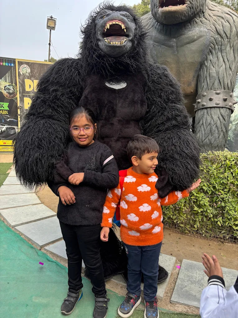 Two young children pose with a large gorilla costume in front of a park backdrop.