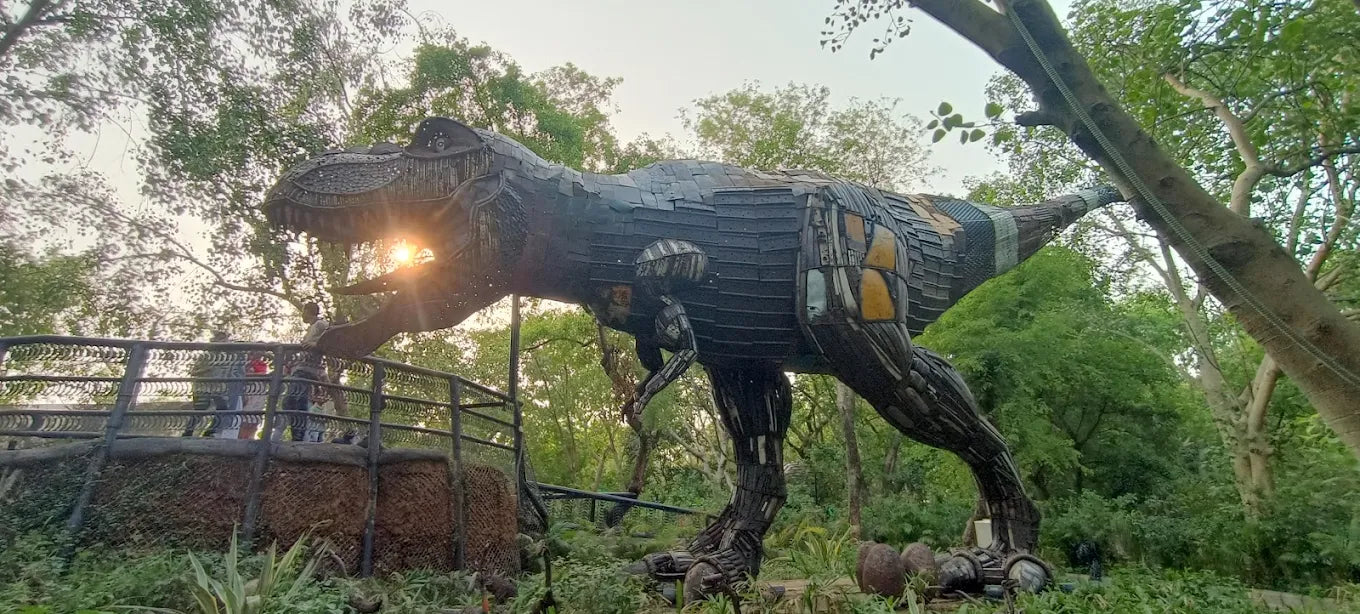 A large dinosaur sculpture made of recycled materials stands in a park with people on a viewing platform.