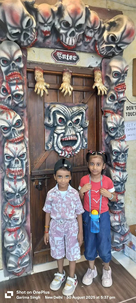 Two children stand in front of a spooky doorway decorated with skulls and severed hands.