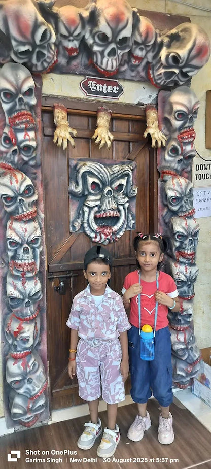 Two children stand in front of a spooky doorway decorated with skulls and severed hands.