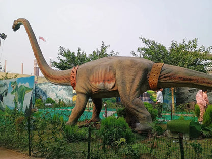 A large dinosaur statue with a long neck stands in a park, with people in the background.
