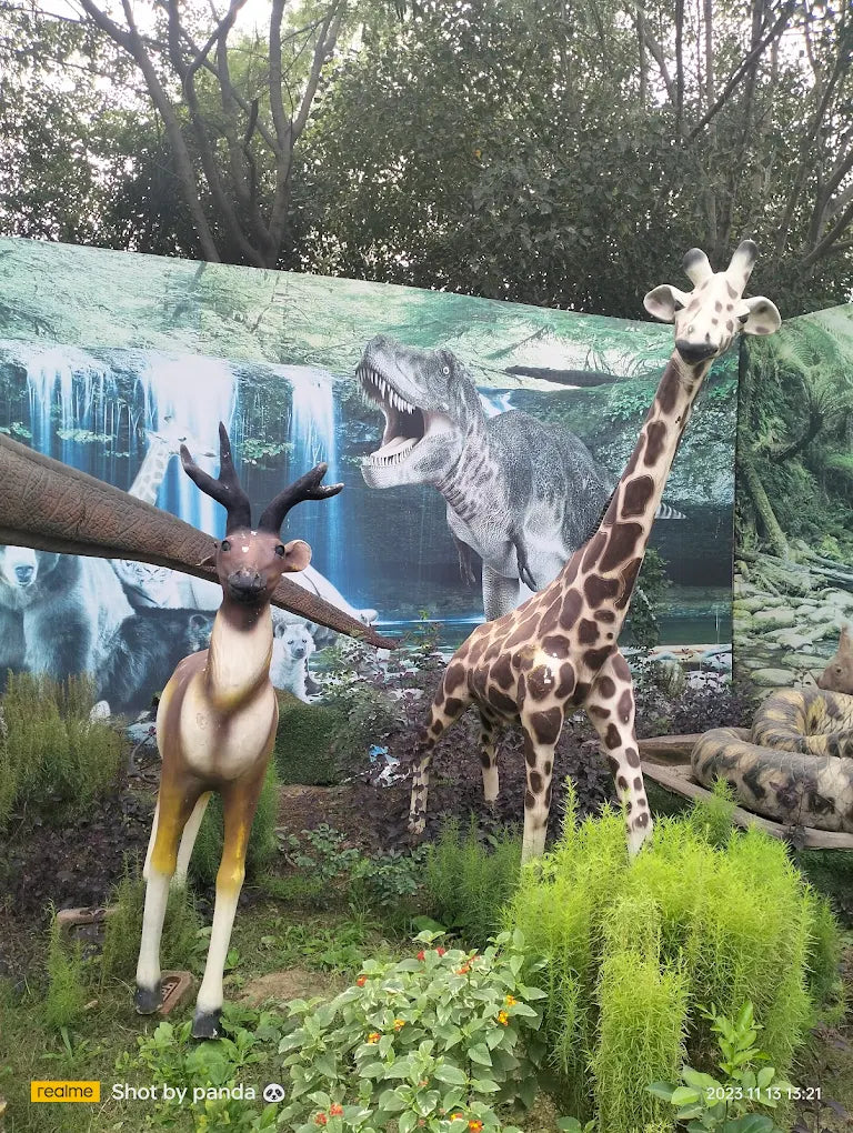 A giraffe and deer statues stand in front of a dinosaur mural.
