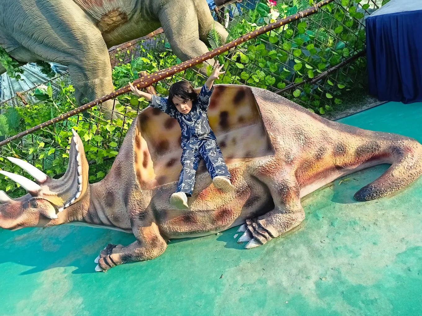 A child sits on a dinosaur statue with arms outstretched.