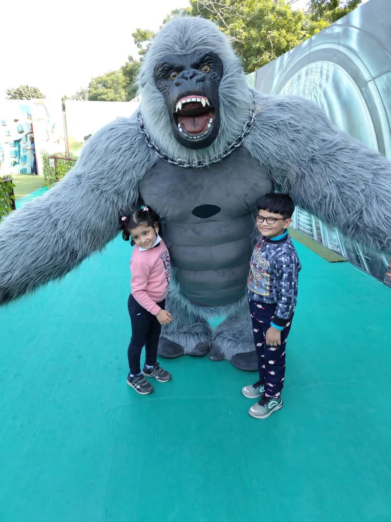 Two young children pose with a large gorilla mascot at an outdoor attraction.