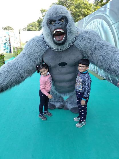 Two young children pose with a large gorilla mascot at an outdoor attraction.